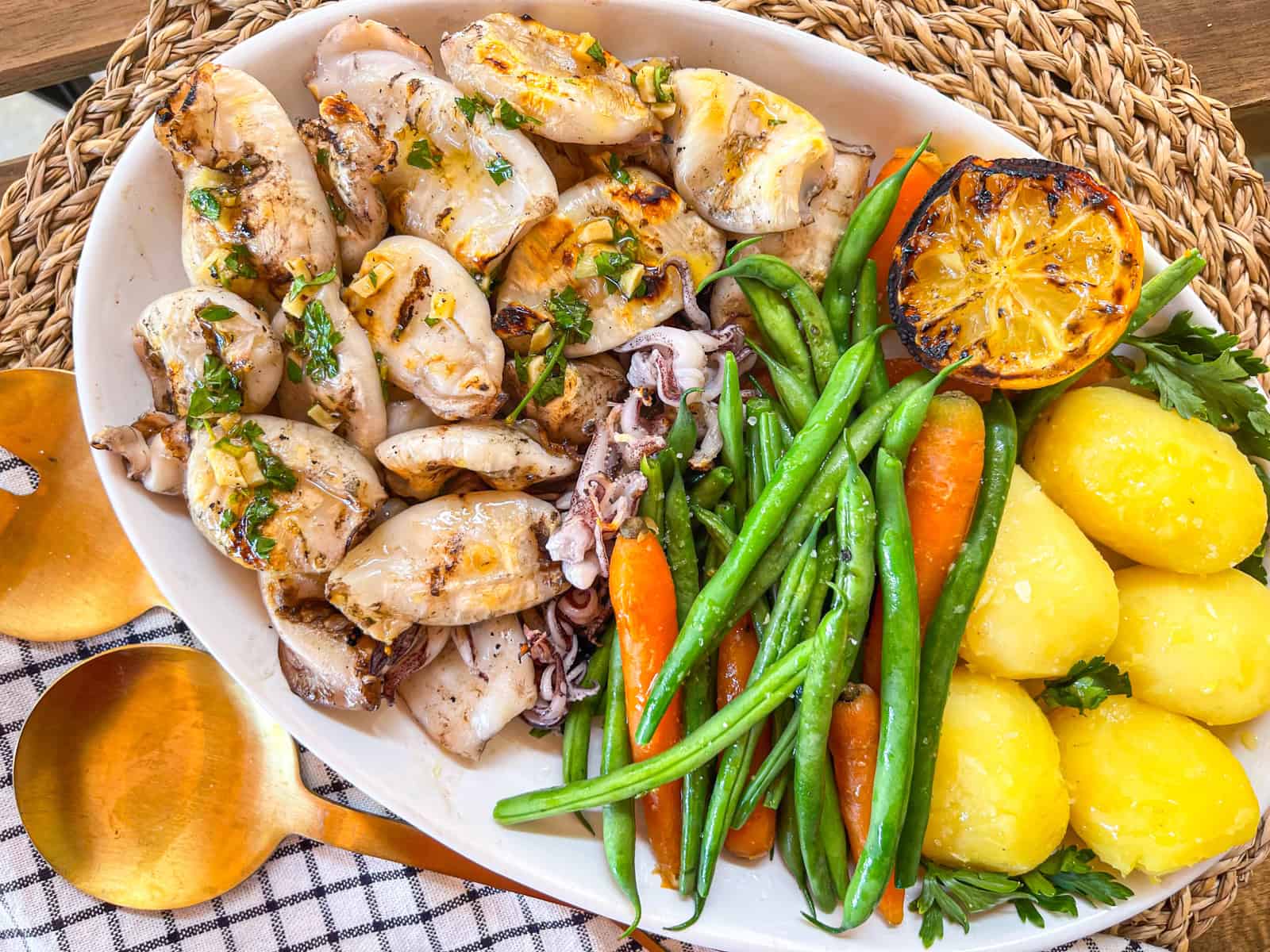 Grilled calamari on a platter served with potatoes and vegetables.