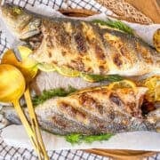 2 whole grilled fish on a platter next to a spoon.