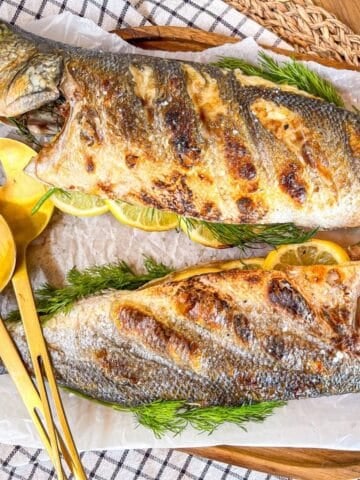 2 whole grilled fish on a platter next to a spoon.