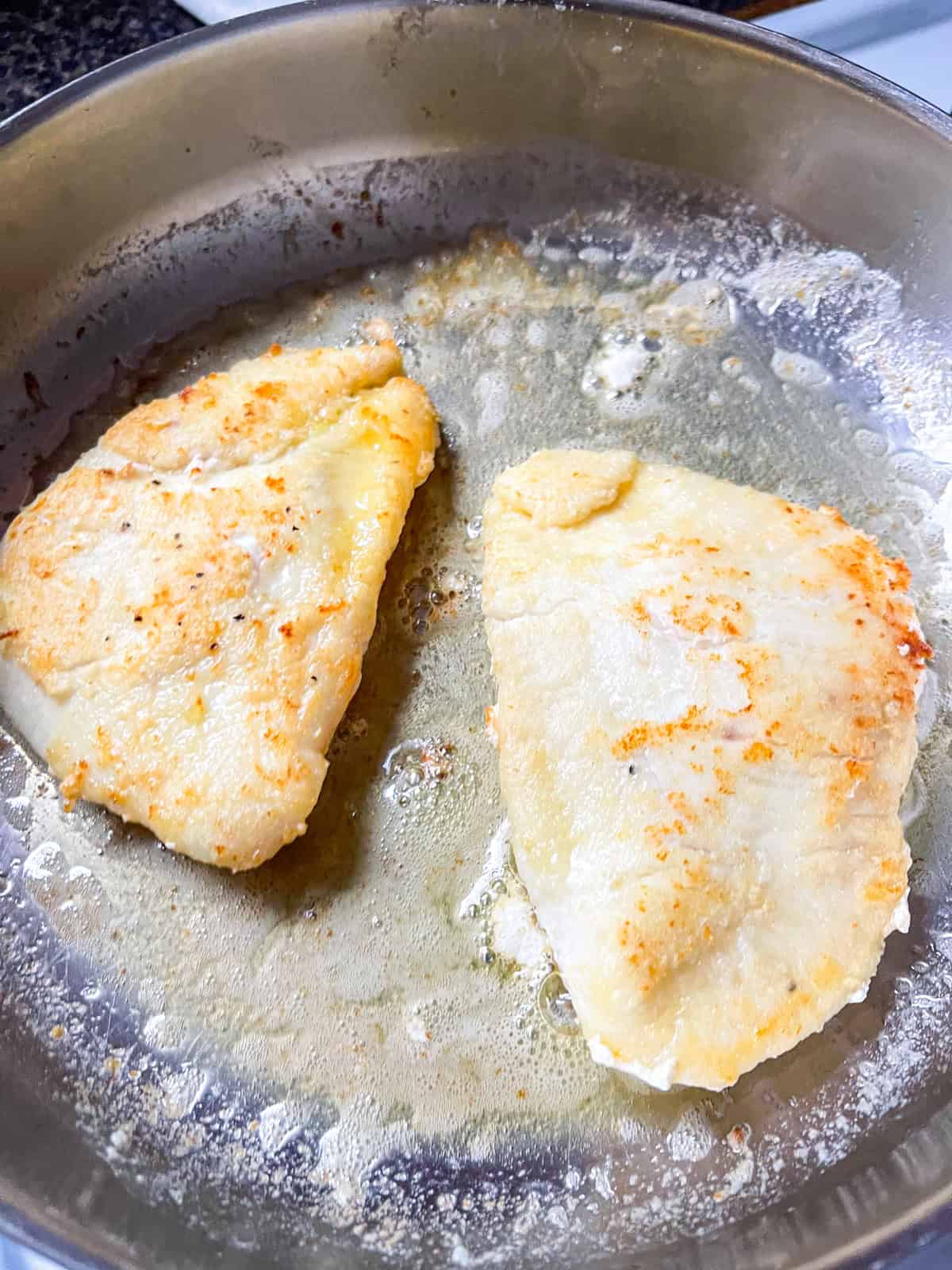 2 pieces of halibut cheeks sauteed in a pan.