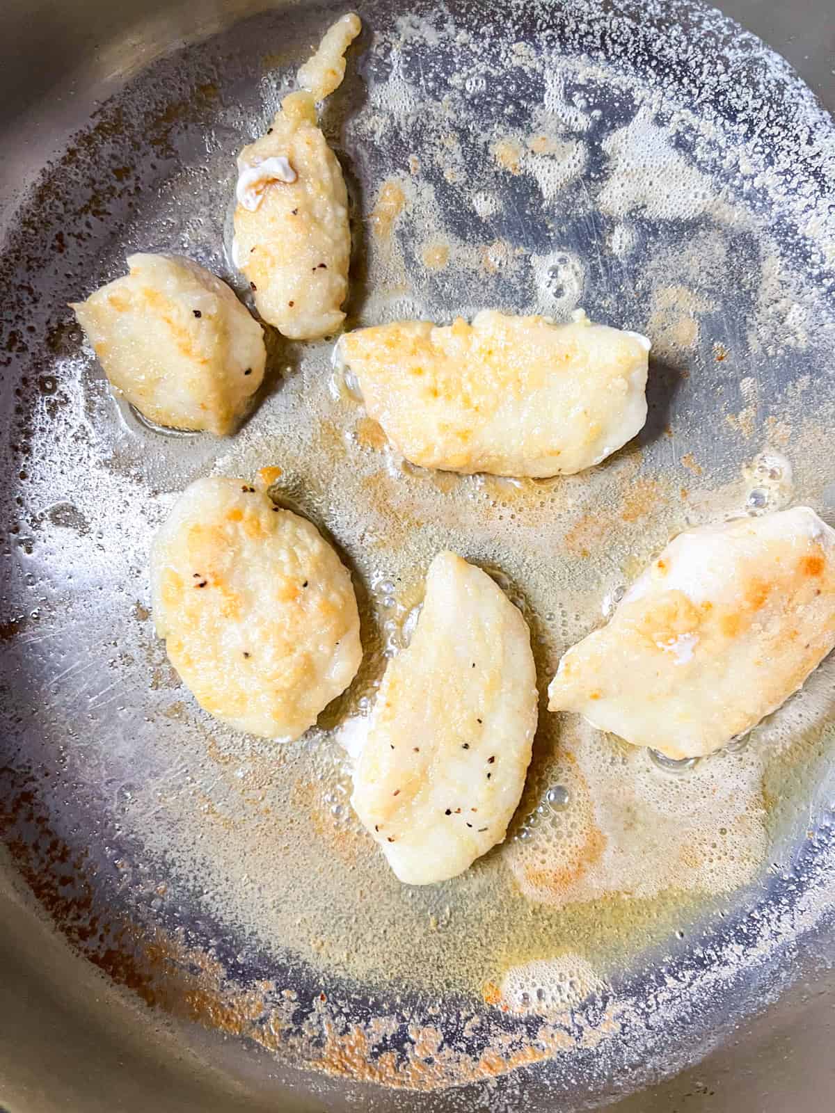 6 small pieces of halibut cheeks sauteed in a pan.