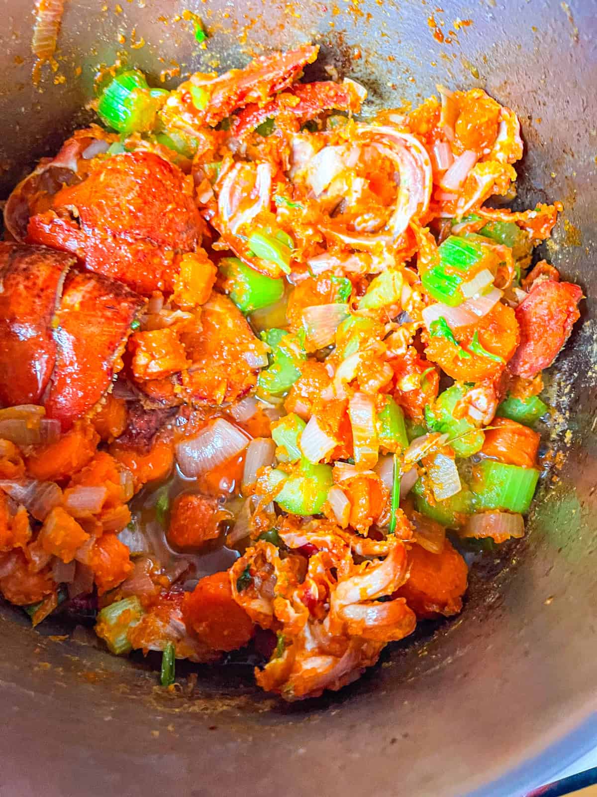 Cook vegetables with crushed lobster shells, garlic, and spices, then stir in tomato paste and cook until it darkens.