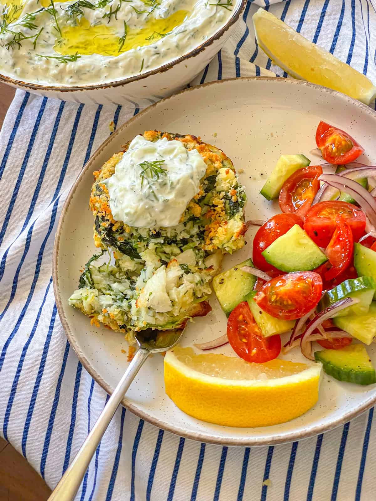 Piece of fish cake with tzatziki on a plate with veegtables.