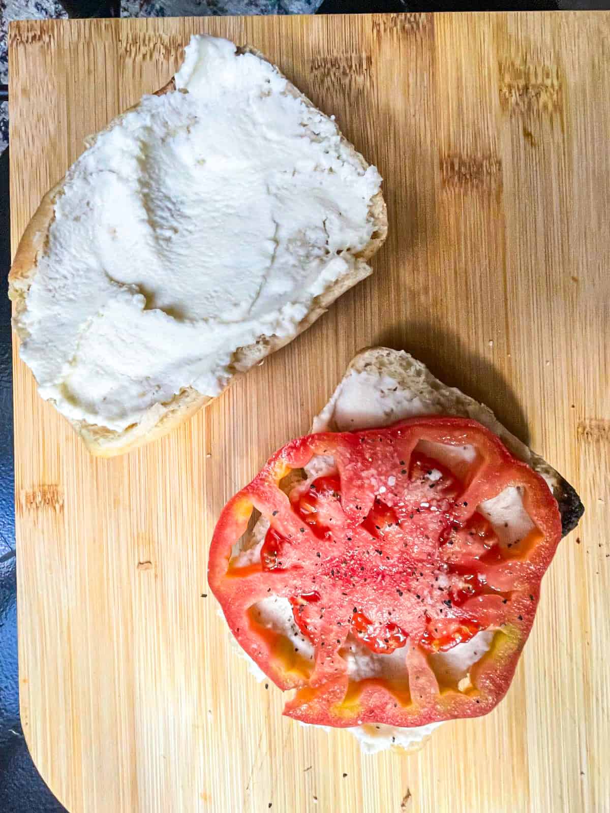 Cream cheese spread over two slices of bread and a slice of seasoned tomato on one piece.