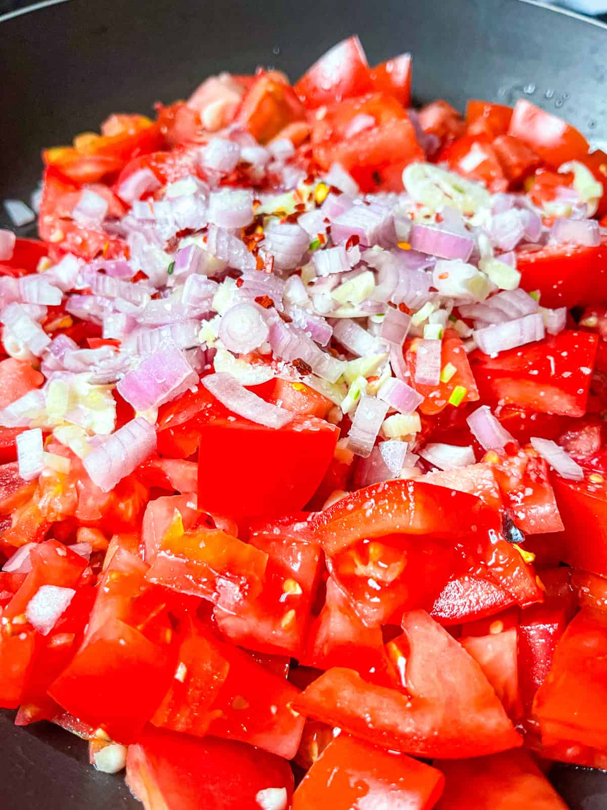Tomatoes, garlic, onions, with spices in a pan.