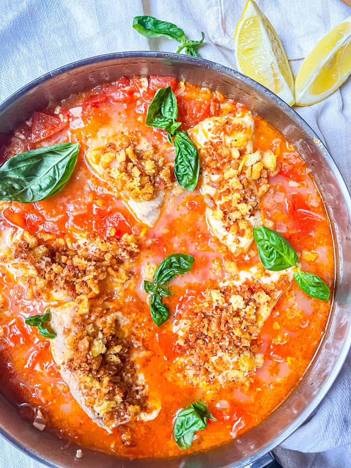 Poached fish in spicy tomato broth in a pan.