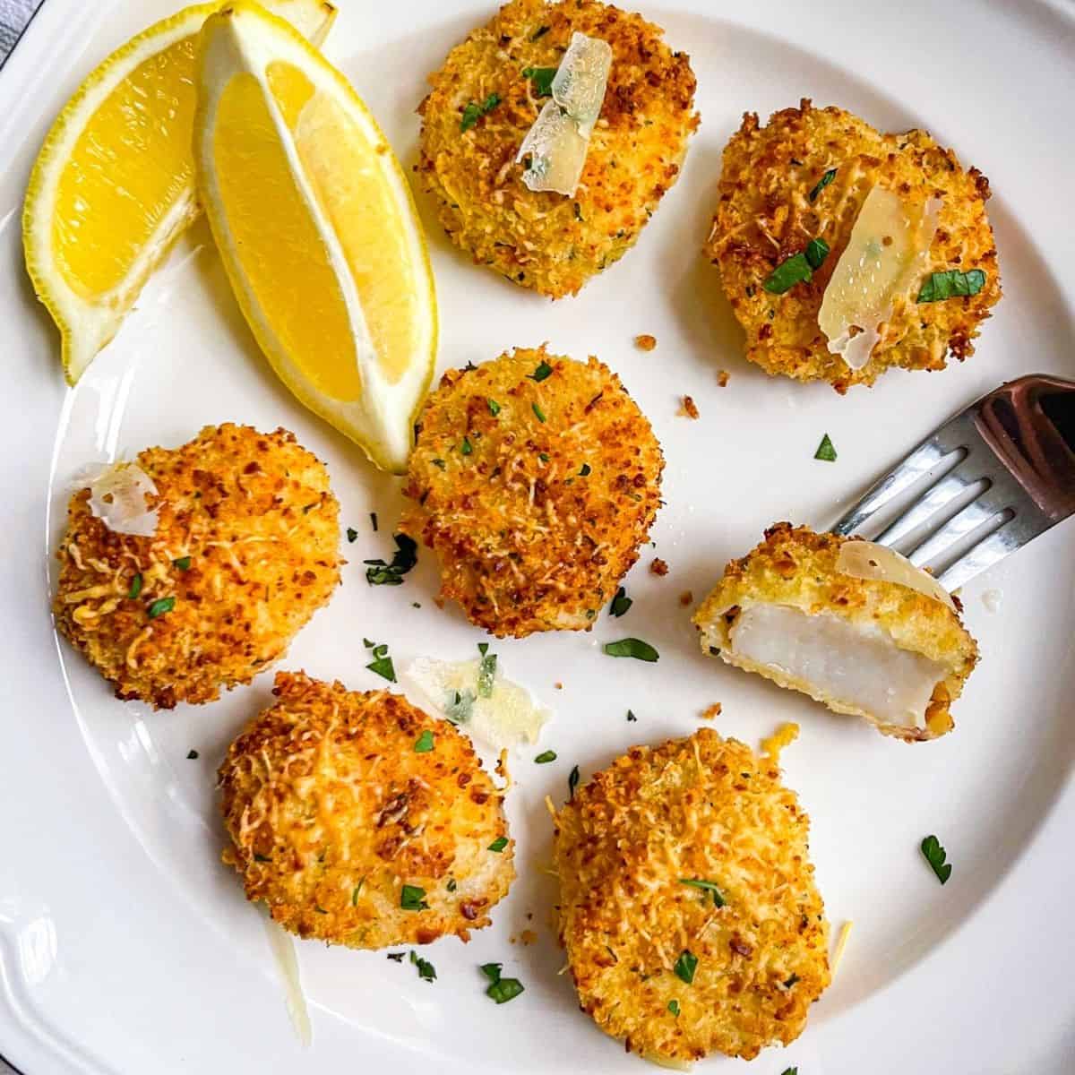 plate of crunchy, coated air fryer sea scallops with panko and parmesan, garnished with two lemon wedges.