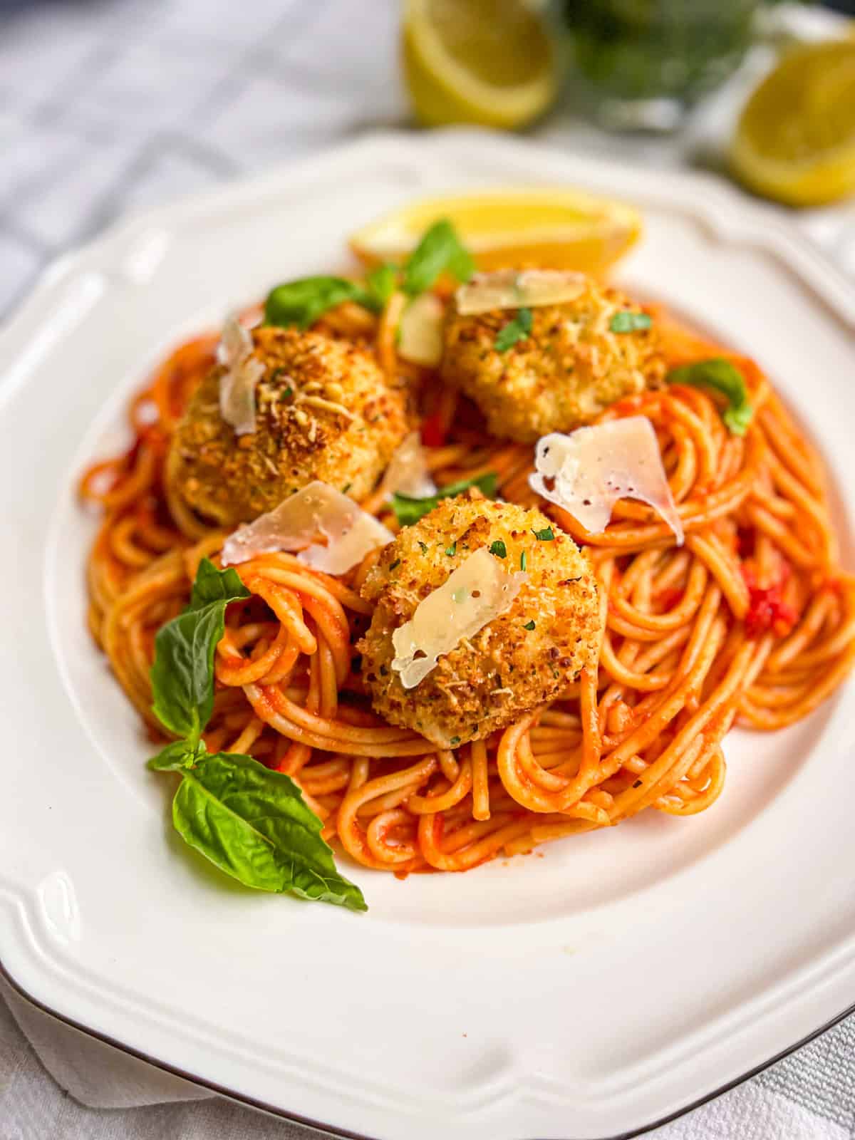 Delicious air fryer scallops served over spaghetti with fresh basil and lemon wedges. 