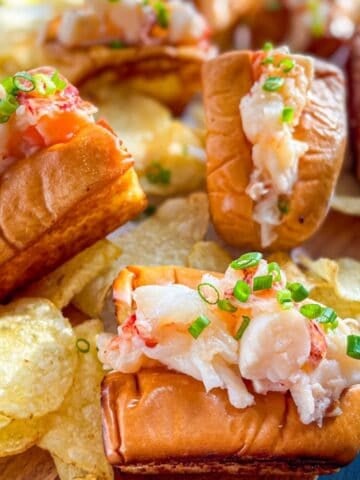 platter of mini lobster rolls topped with chives and served with potato chips.