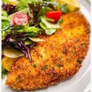 crispy halibut cheeks served on a white plate with a tossed salad, parmesan and lemon wedges.