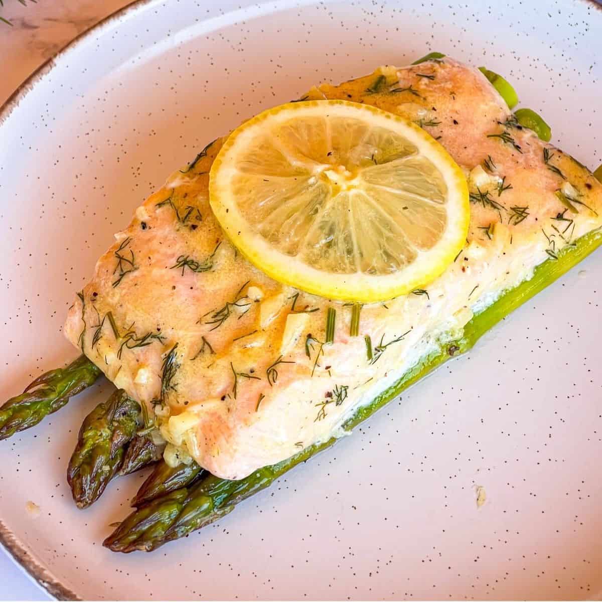 Salmon over asparagus with sauce and lemon slices.