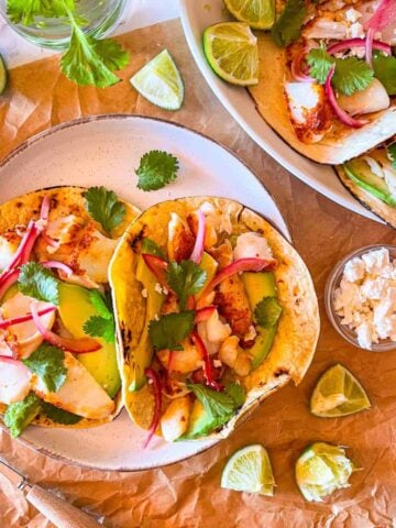 Fish tacos on plates on a board.
