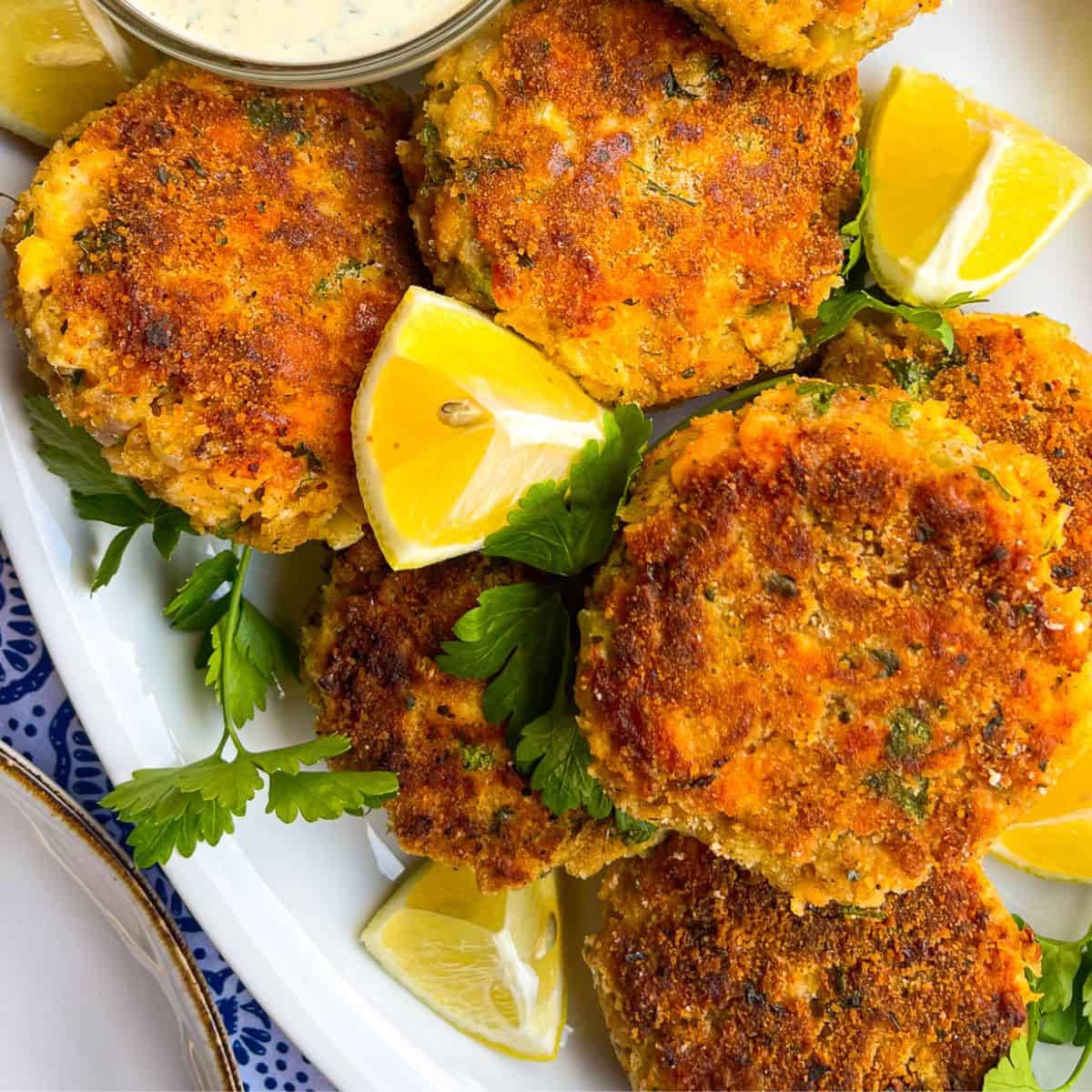 Salmon Patties on a platter with lemons and sauce.