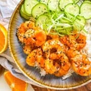 Teriyaki Shrimp in a bowl with rice, scallion strings and cucumbers.