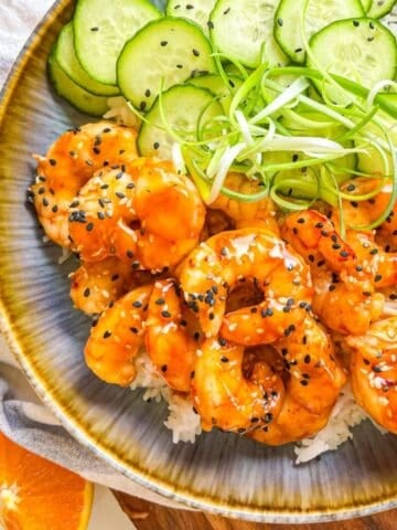 Teriyaki Shrimp in a bowl with rice, scallion strings and cucumbers.