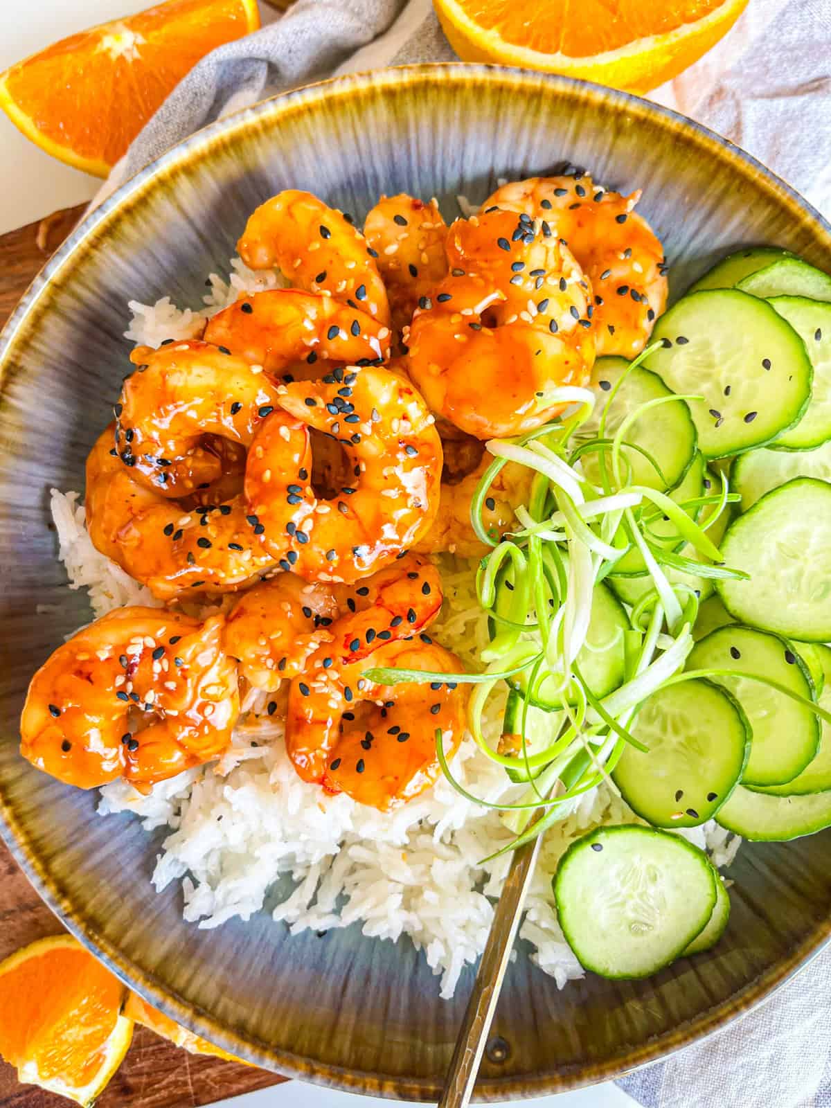 Teriyaki Shrimp in a bowl with rice, scallion strings and cucumbers.