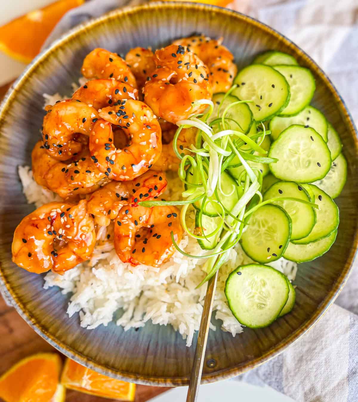 Teriyaki Shrimp in a bowl with rice, scallion strings and cucumbers.
