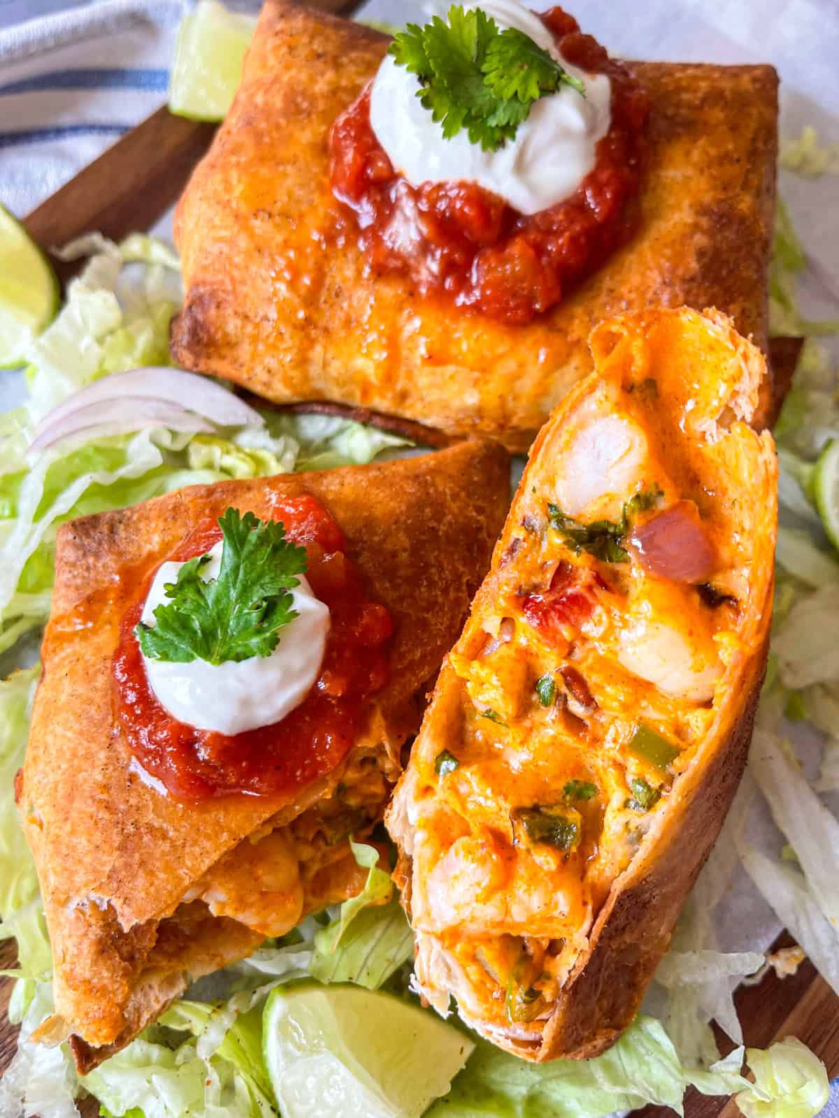 Air fryer shrimp chimichanga cut open on a platter with limes, salsa and sour cream.