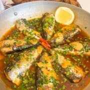 Portuguese garlic sardines in a sauce with cilantro, garlic and garnished with lemon.