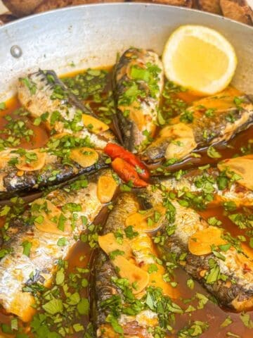 Portuguese garlic sardines in a sauce with cilantro, garlic and garnished with lemon.