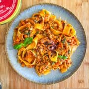 octopus pasta in a shallow bowl, pappardelle coated in tomato ragu with torn basil and Parmesan.