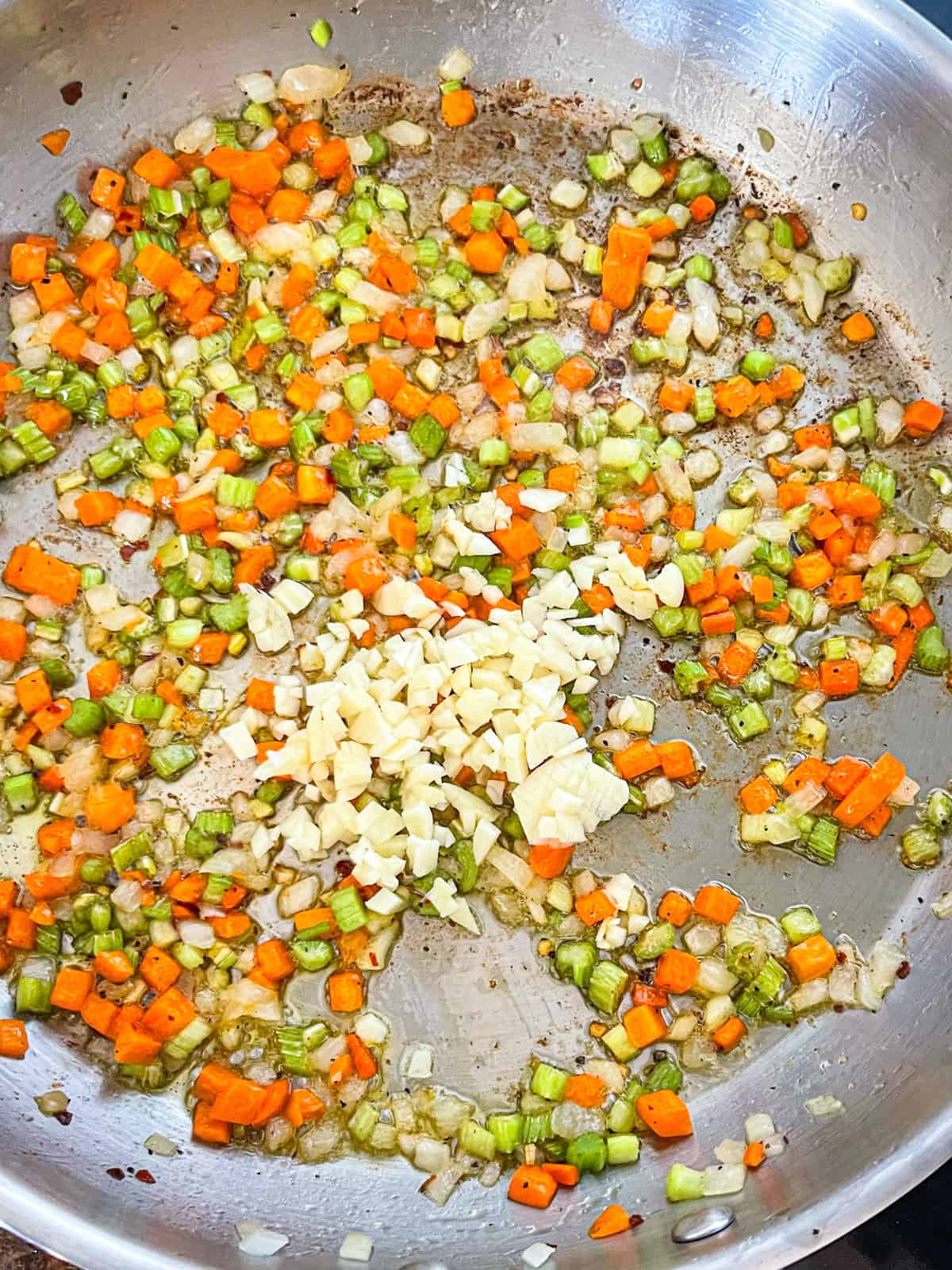 soffritto of onion, carrot, and celery cooking in oil from the octopus tins.