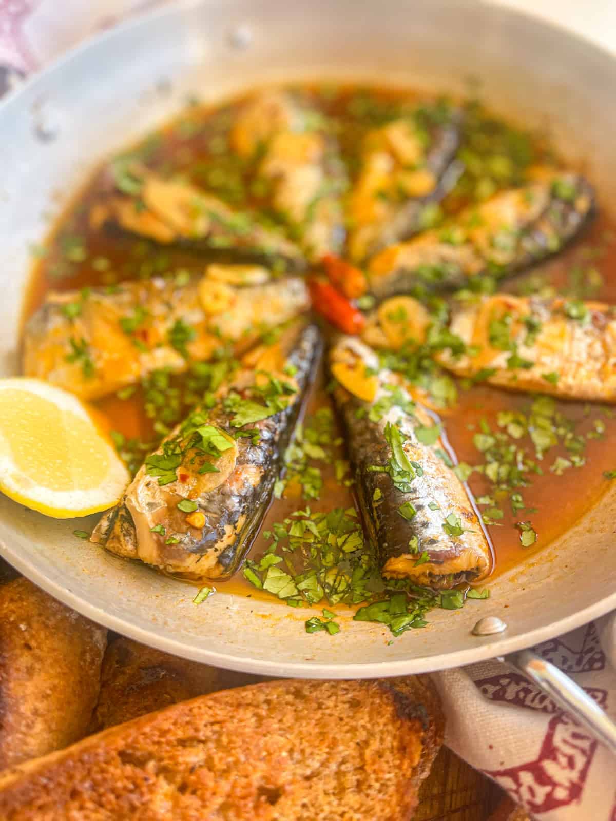 Portuguese garlic sardines in a sauce with cilantro, garlic and garnished with lemon.
