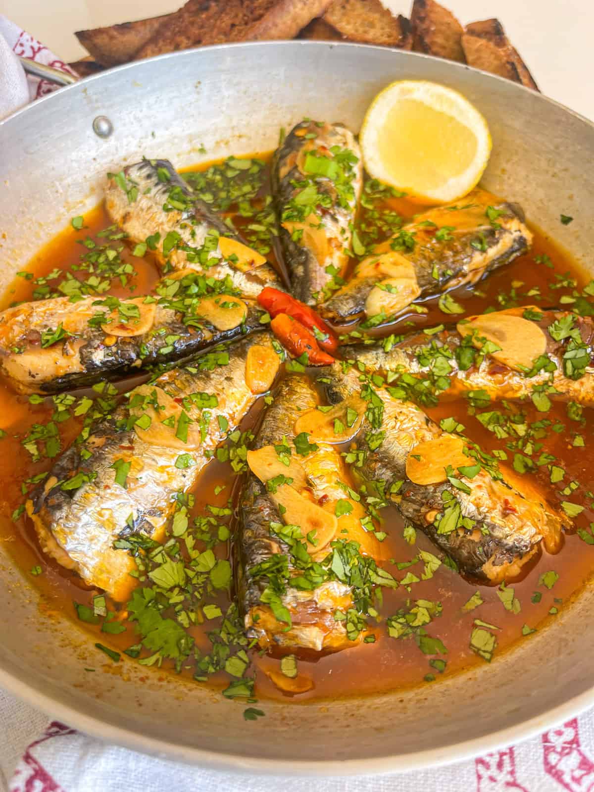 Portuguese garlic sardines in a sauce with cilantro, garlic and garnished with lemon.